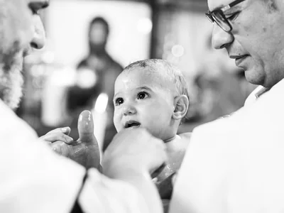 Kind blickt nach der Tonsur zwischen Priester und Vater in der Kreuzerhöhungskirche Rüsselsheim
