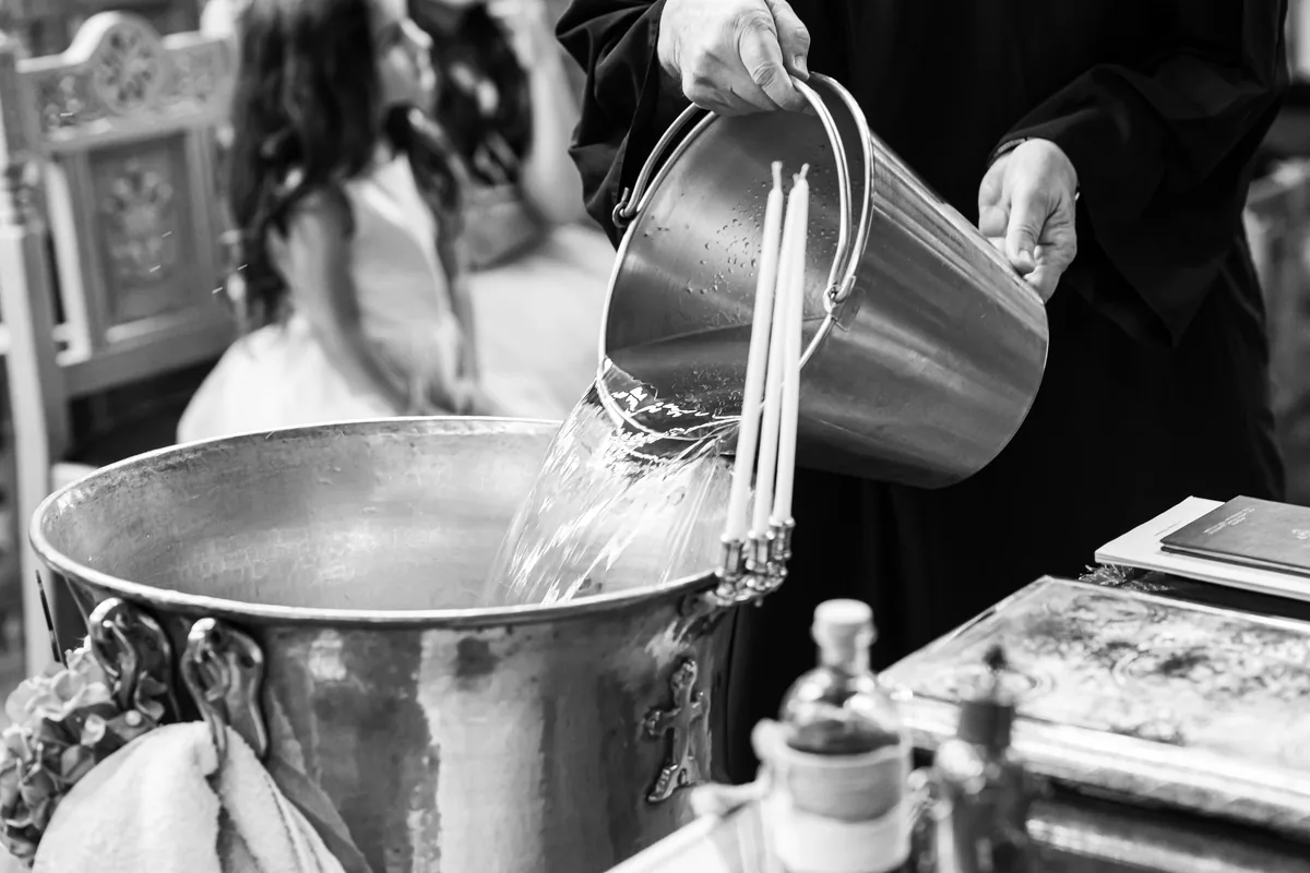 Priester füllt Wasser in das Taufbecken