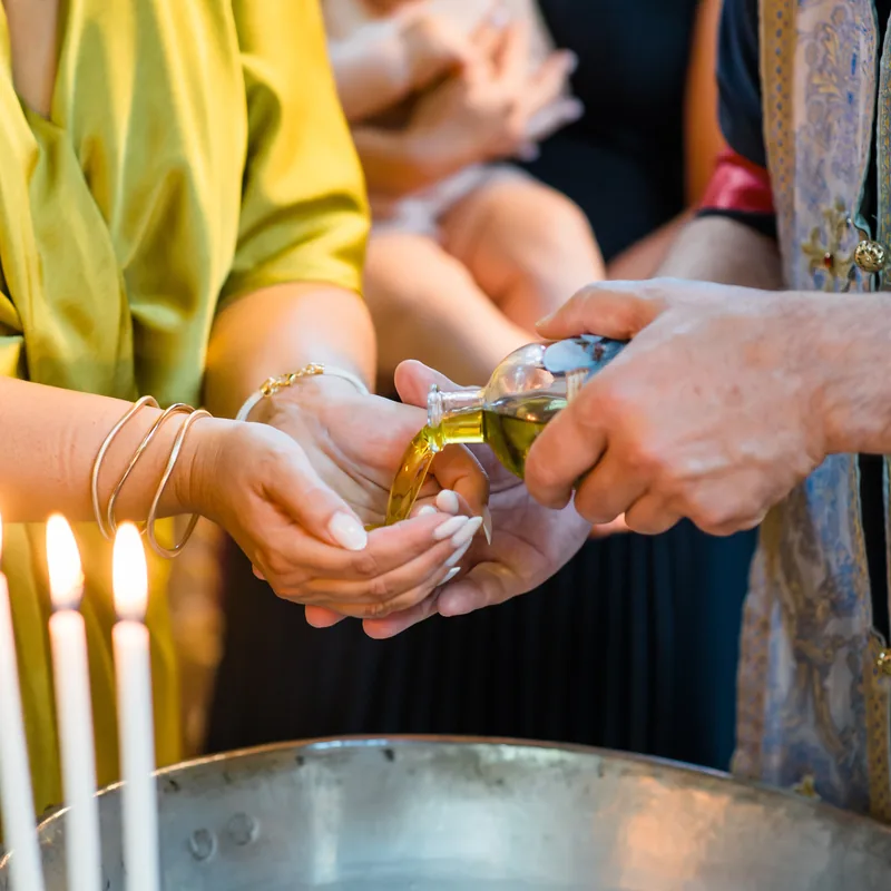 Priester gießt geweihtes Olivenöl in die Hände vor der Salbung