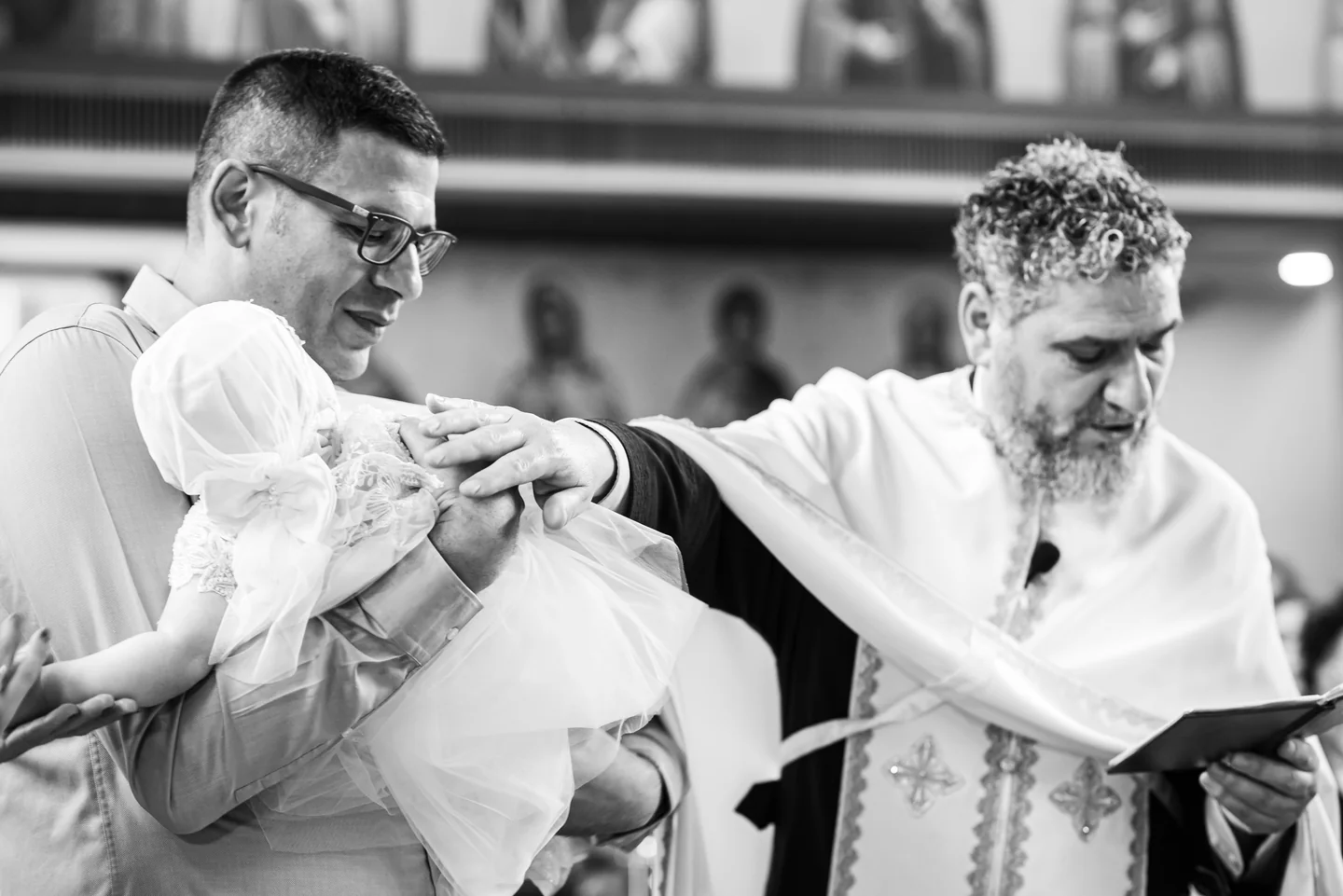 Priester berührt die Hand des Kindes im weißen Taufkleid während der Zeremonie